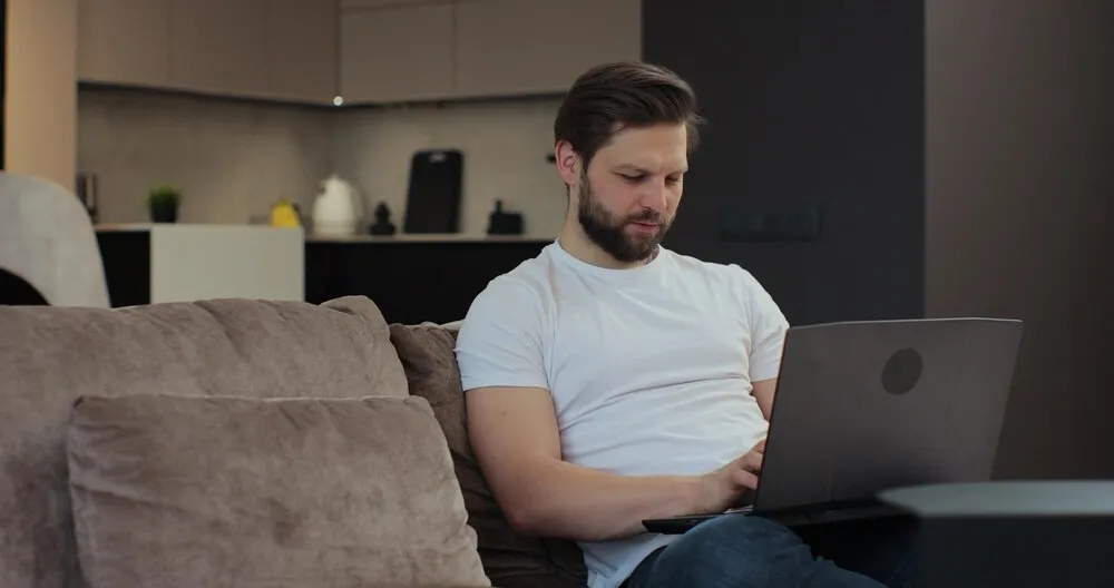 mężczyzna w swobodnym stroju siedzący na kanapie w salonie i korzystający z laptopa mężczyzna pracujący z domu zakupy online nowoczesna technologia koncepcja internetu i ludzi