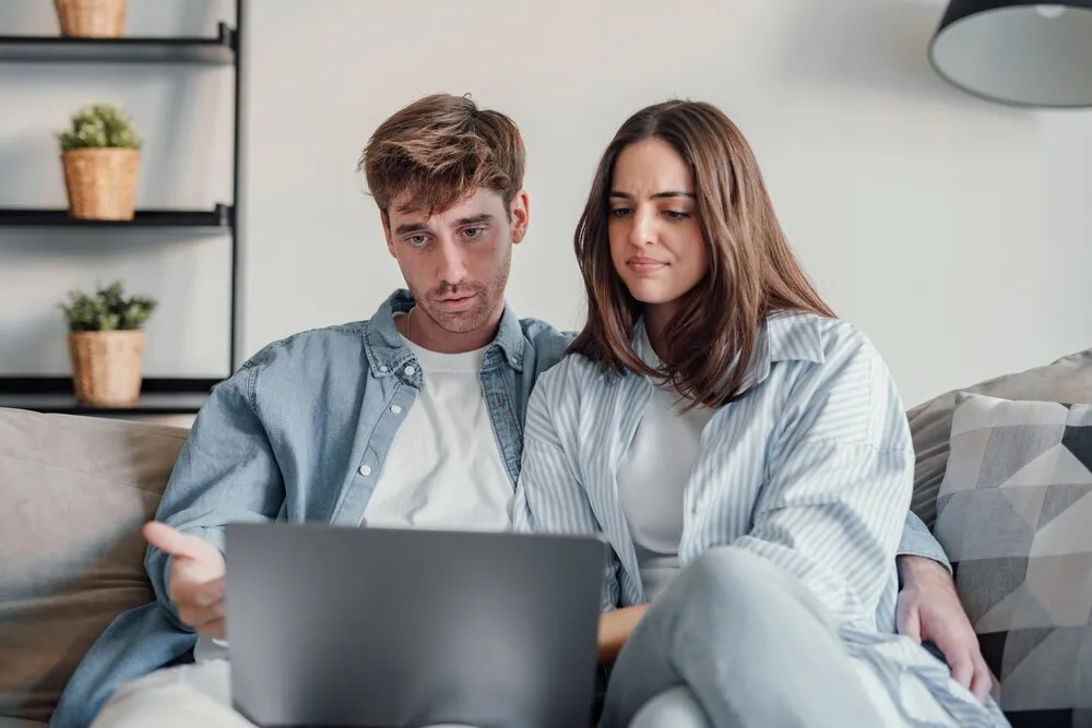 para milenialsów zirytowana zawieszonym laptopem lub wiadomościami online siedząca razem na kanapie sfrustrowani młodzi gniewni klienci skonsternowani problemem z komputerem czujący zmieszanie lub zakłopotanie z powodu wiadomości e-mail