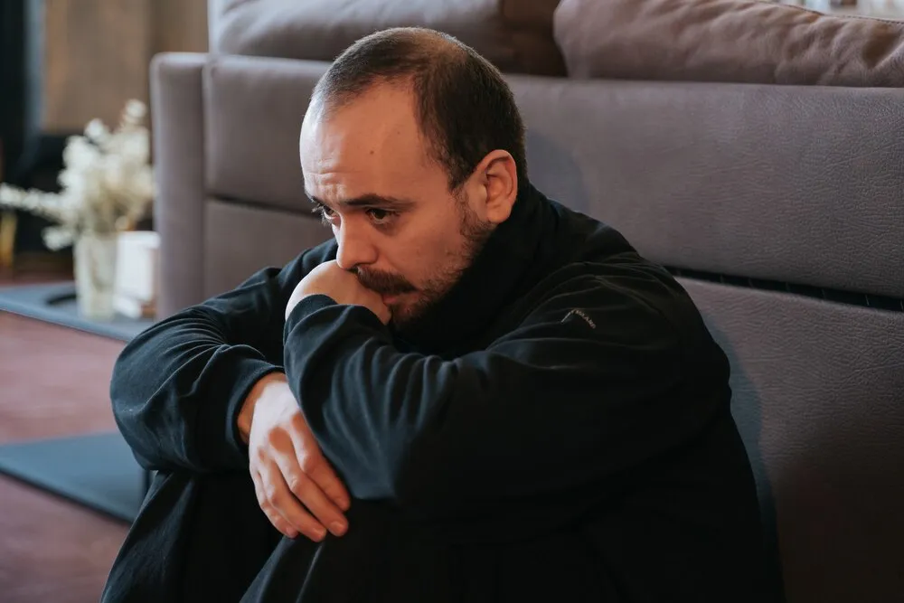 młody mężczyzna w depresji, zmartwiony i smutny, brodaty. siedzi sam