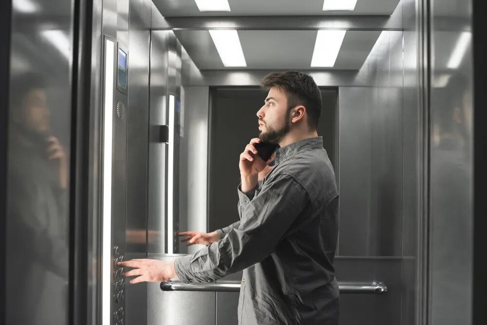 Biznesmen rozmawia przez telefon w windzie i naciska przycisk.