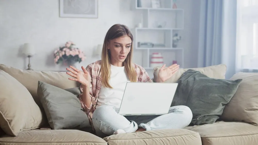 zdezorientowana kobieta gestykulująca podczas korzystania z laptopa na sofie w domu